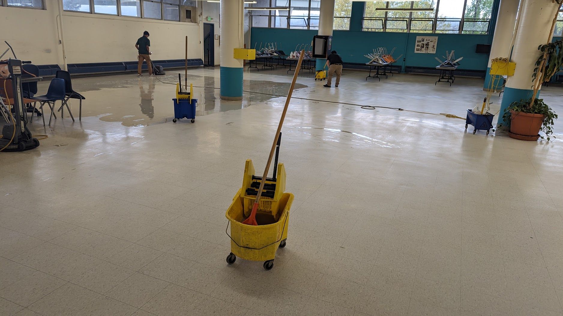 Yellow mop bucket with wringer and mop in a shiny gymnasium floor