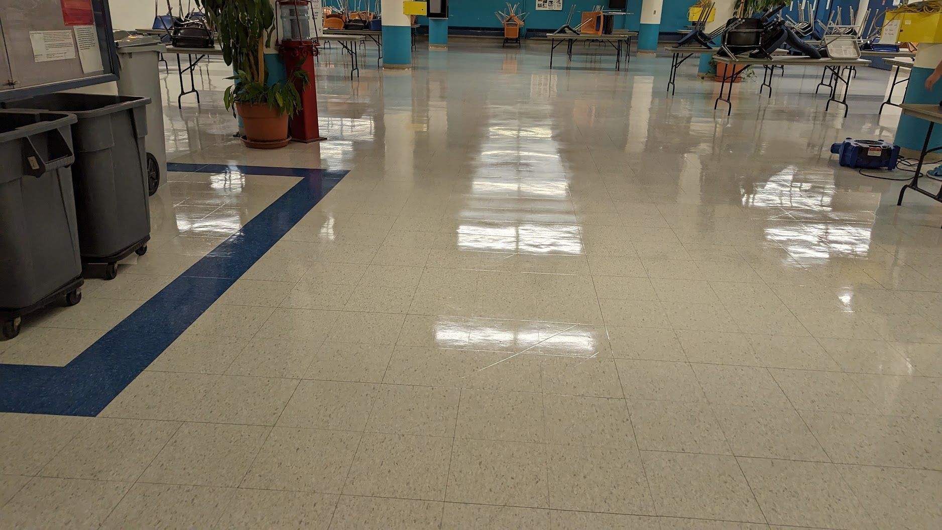 Empty school hallway with glossy tile floor and blue border lines, chairs and tables in the background