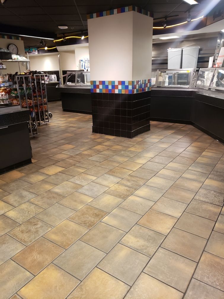 Empty restaurant dining area with tiled floor, black counters, and a white column with colorful mosaic trim