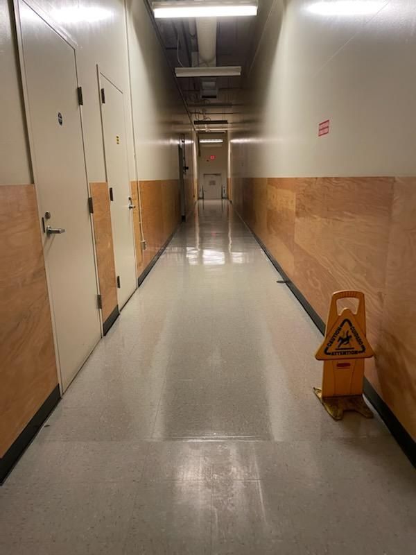 Empty hallway with beige walls, double doors, and a yellow wet floor caution sign.