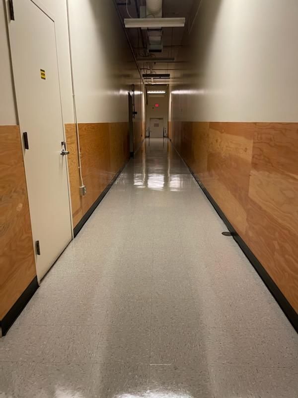 Long, empty hallway with beige walls, white floor, and doors along the left side.