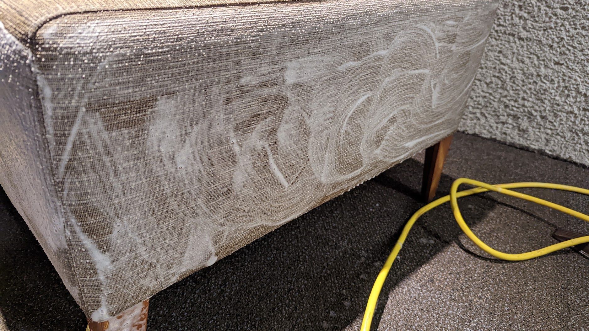 Gray upholstered bench with white scribble markings, standing on carpet beside a yellow cord