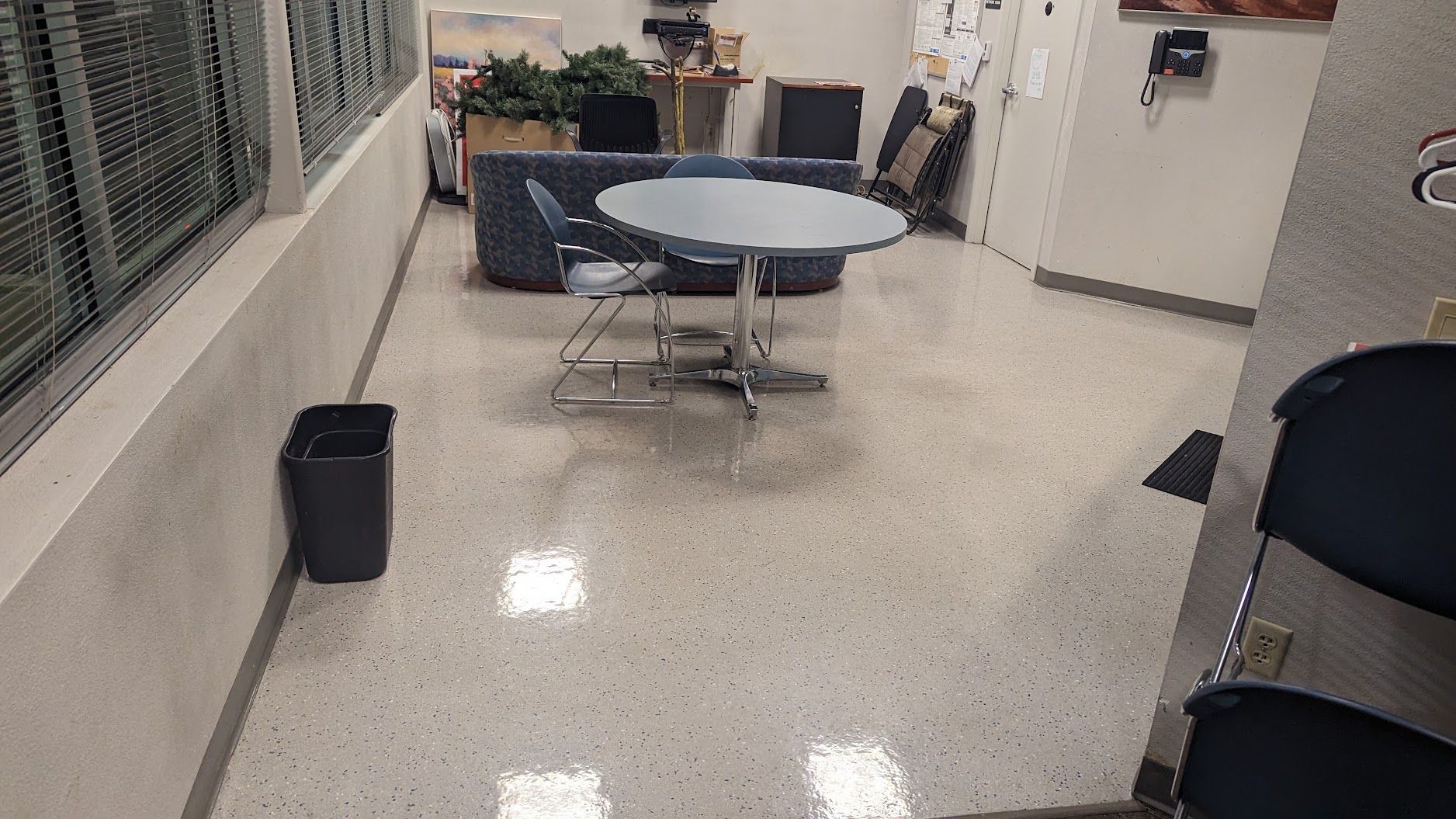 Break room with round table, chairs, trash can, and cabinets on a speckled floor.