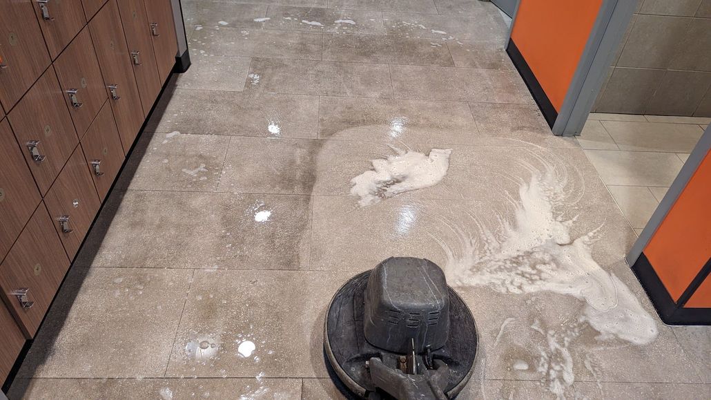 Hallway floor with a black floor drain and scattered white dust near orange and brown cabinets