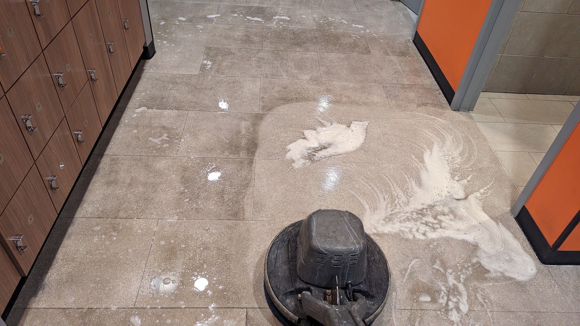 Hallway floor with a black floor drain and scattered white dust near orange and brown cabinets