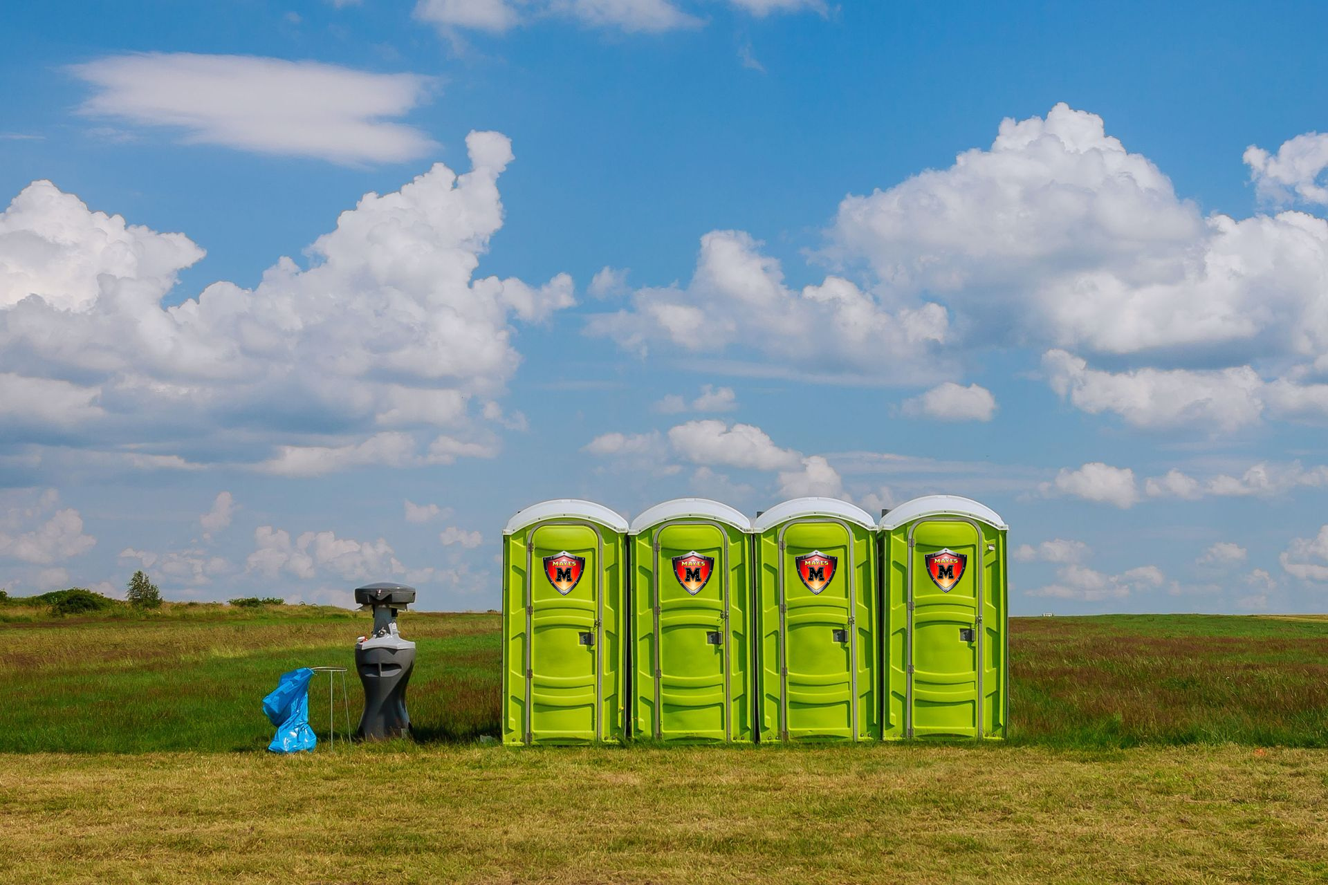 A man in a neon vest near a blue porta-potty in a grassy field; bulldozer in background.