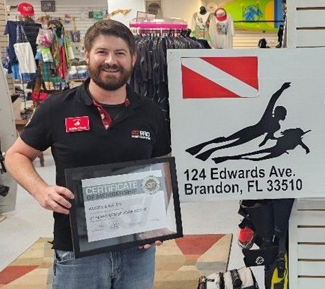 A man is holding a certificate in front of a sign that says 124 edwards ave brandon fl 33510