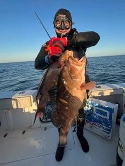 A man in a wet suit is holding a large fish on a boat.