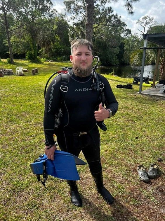 A man in a wet suit is holding a pair of flippers and giving a thumbs up.