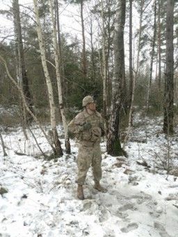 A soldier is standing in the snow in the woods.