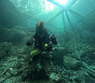 A scuba diver is standing on a rock in the water.