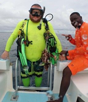 A man in a yellow shirt is standing on a boat next to another man in orange shorts