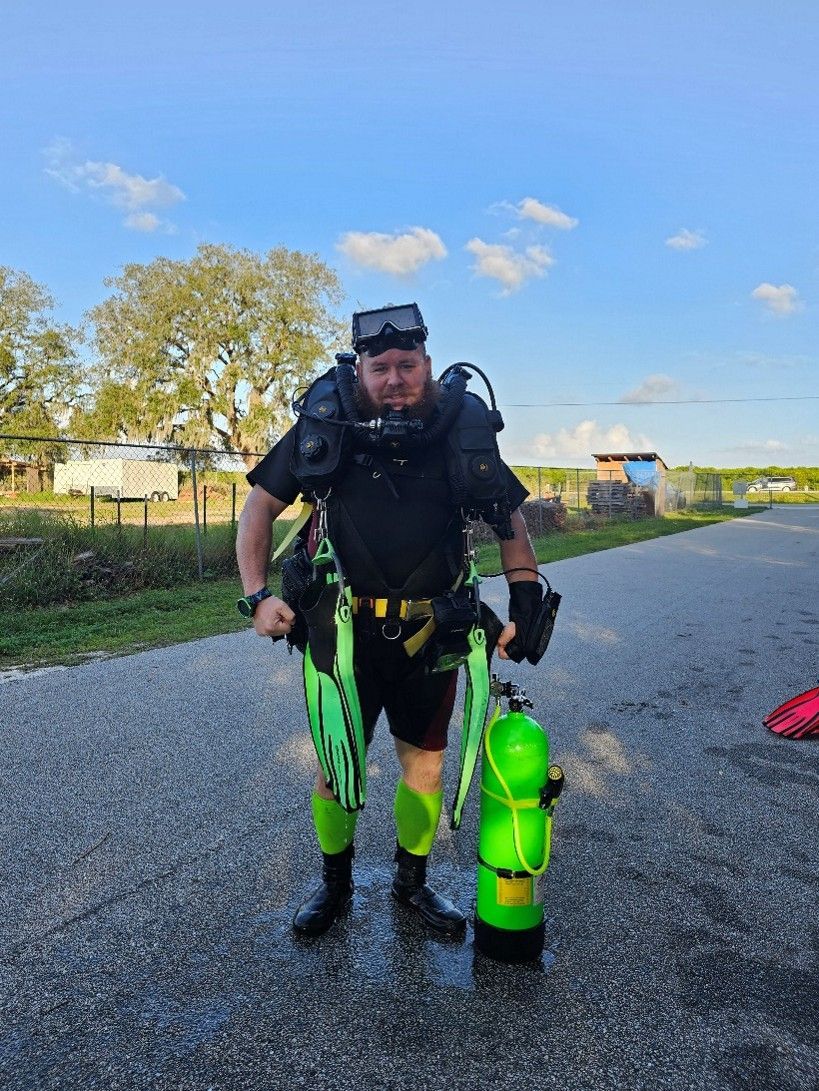 A man in a scuba suit is standing on the side of the road holding a scuba tank.