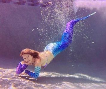 A woman in a mermaid costume is swimming underwater in a pool.