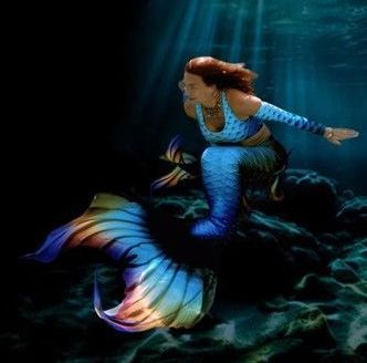A woman in a mermaid costume is swimming underwater