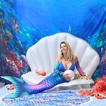 A woman dressed as a mermaid is sitting on a shell couch.
