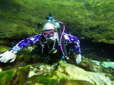 A scuba diver is swimming in the water near a rock.