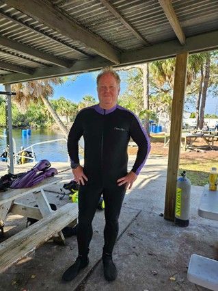 A man in a wetsuit is standing under a canopy next to a picnic table.