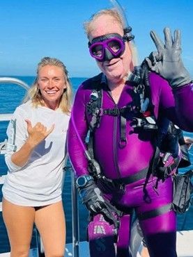A man in a purple wetsuit is standing next to a woman on a boat.