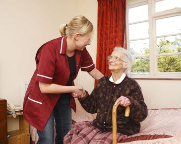 Staff member helping woman stand up from her bed