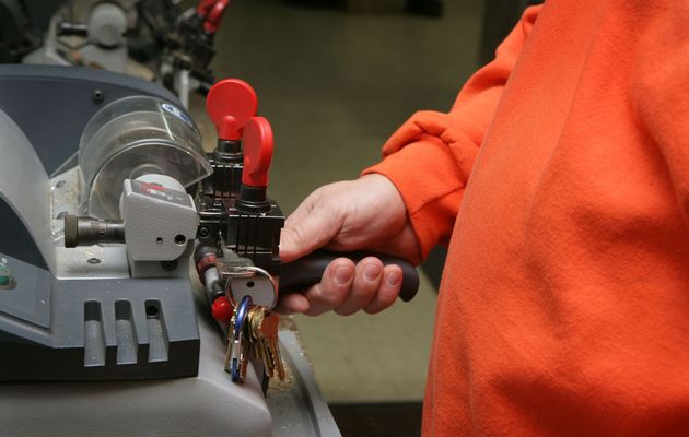 Person in orange jacket using a key machine to cut keys with a red handle and metal tray