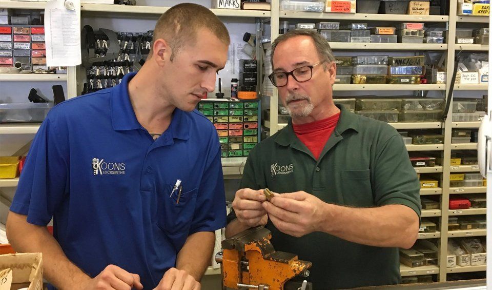 Two men examining a small part at a workbench in a hardware store aisle