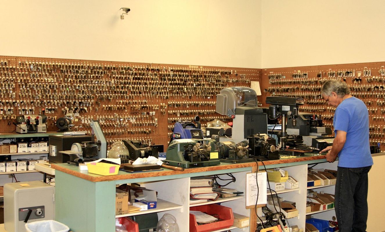 Large workshop with shelves of parts and a person in a blue shirt working at a cluttered counter.