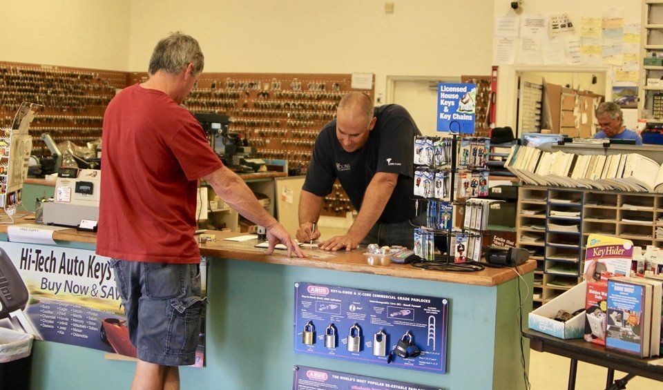 Two men behind a counter in a model train shop, examining items with shelves of parts in the background.