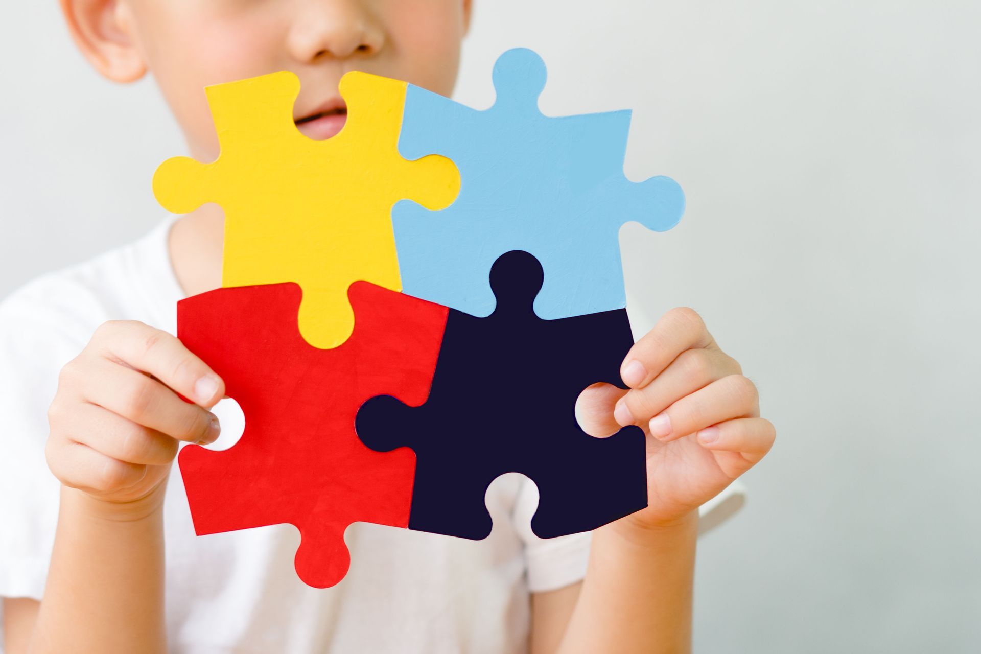 Boy holding four colorful puzzle pieces: red, yellow, blue, and navy.
