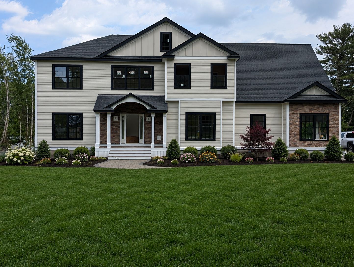 Large two-story suburban house with gray siding, black roof, and a green front lawn