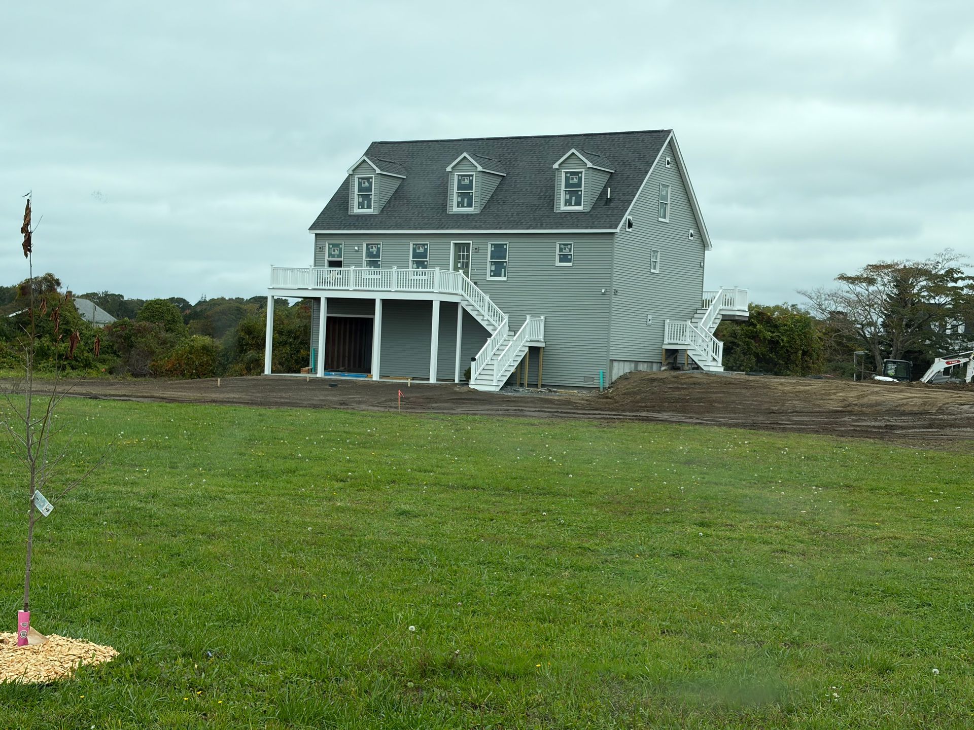 Gray house with white porch and stairs on a grassy lot under an overcast sky