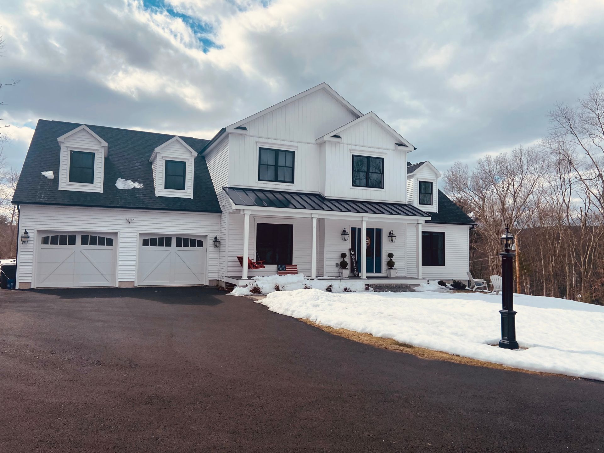 White farmhouse-style house with black accents, front porch, and driveway. Snow on the ground.