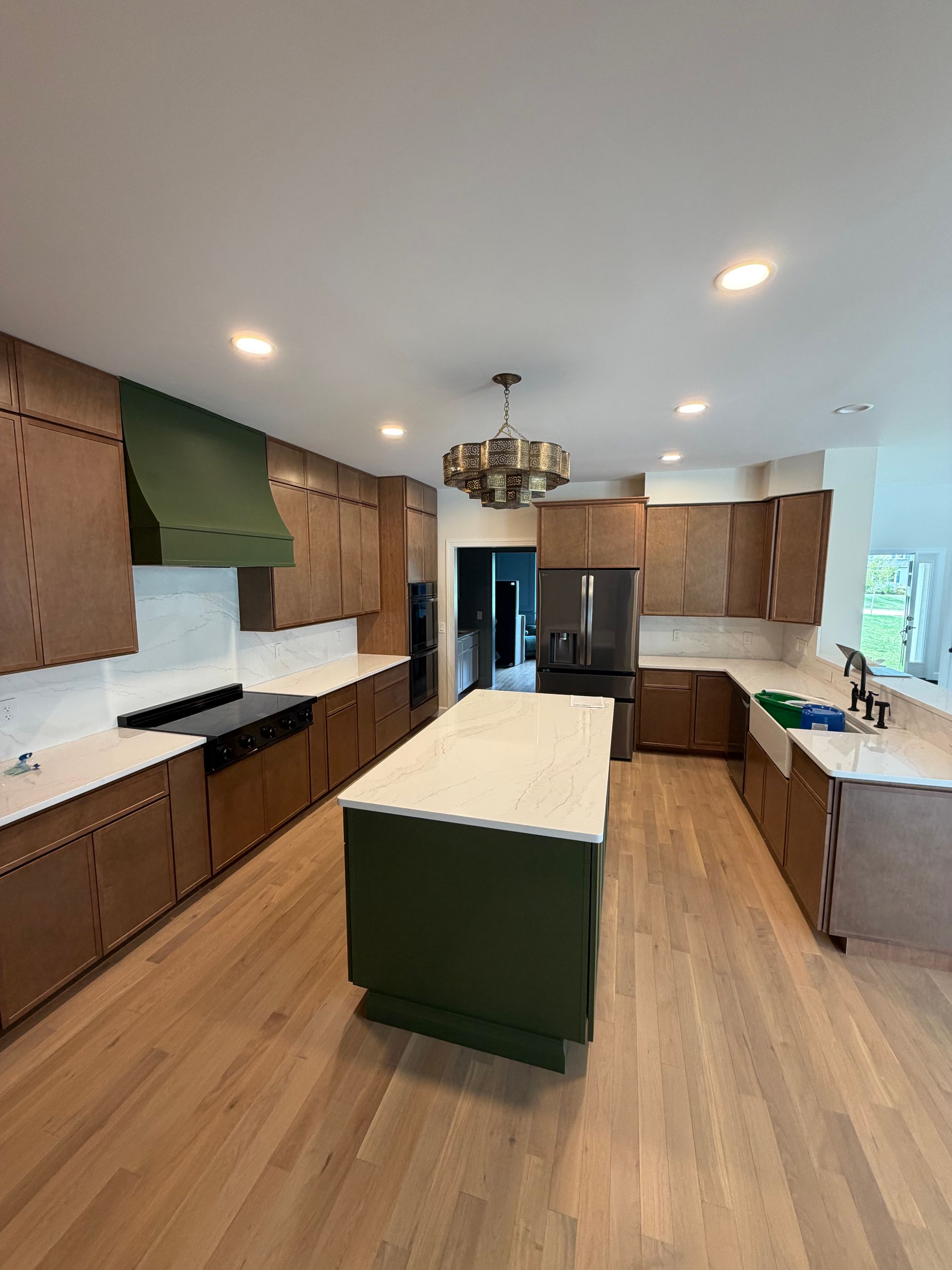 Modern kitchen with wood cabinets, white island, stainless fridge, green accents, and recessed lighting.