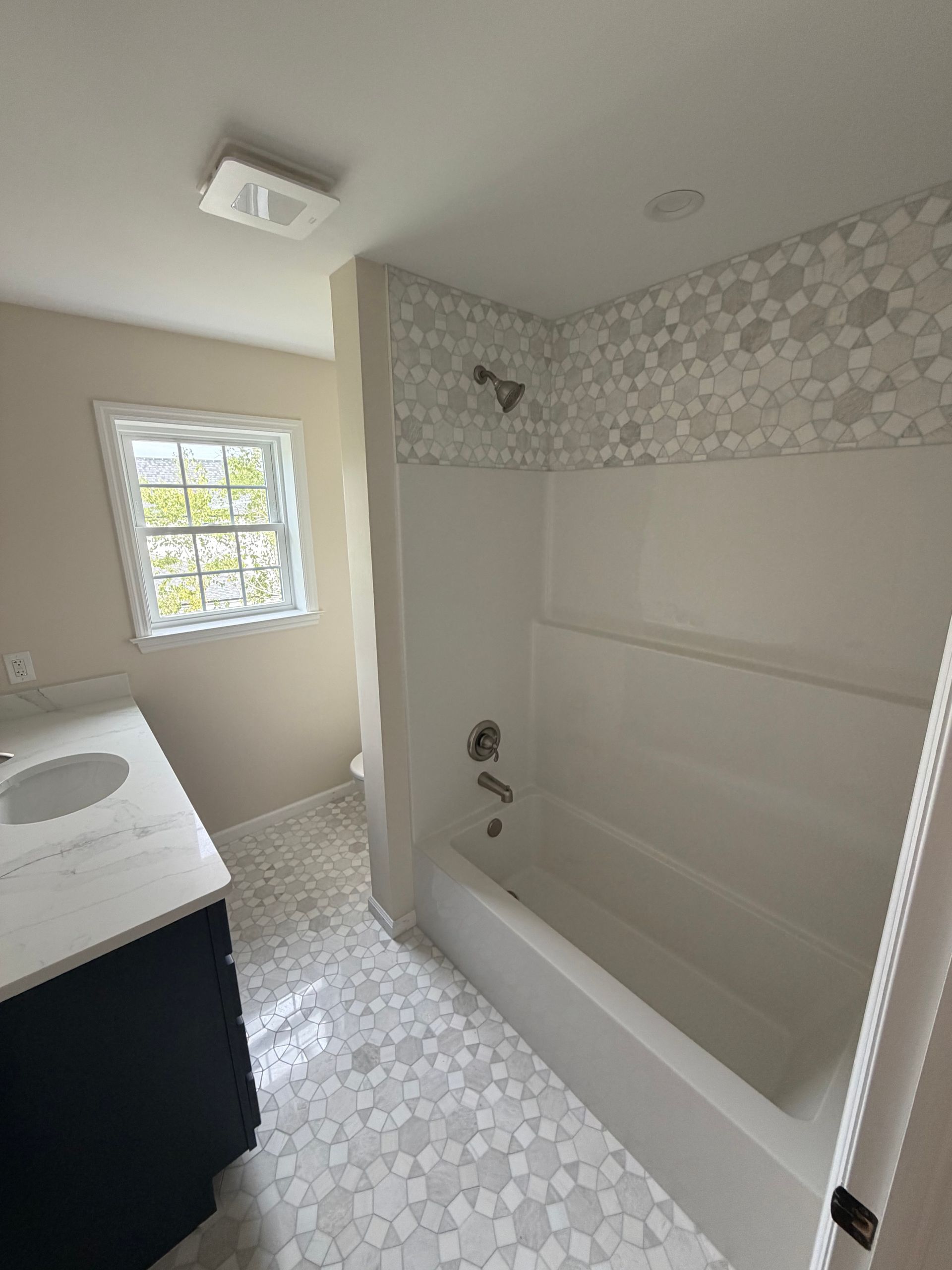 Small bathroom with white tile, vanity, window, and bathtub/shower combo.