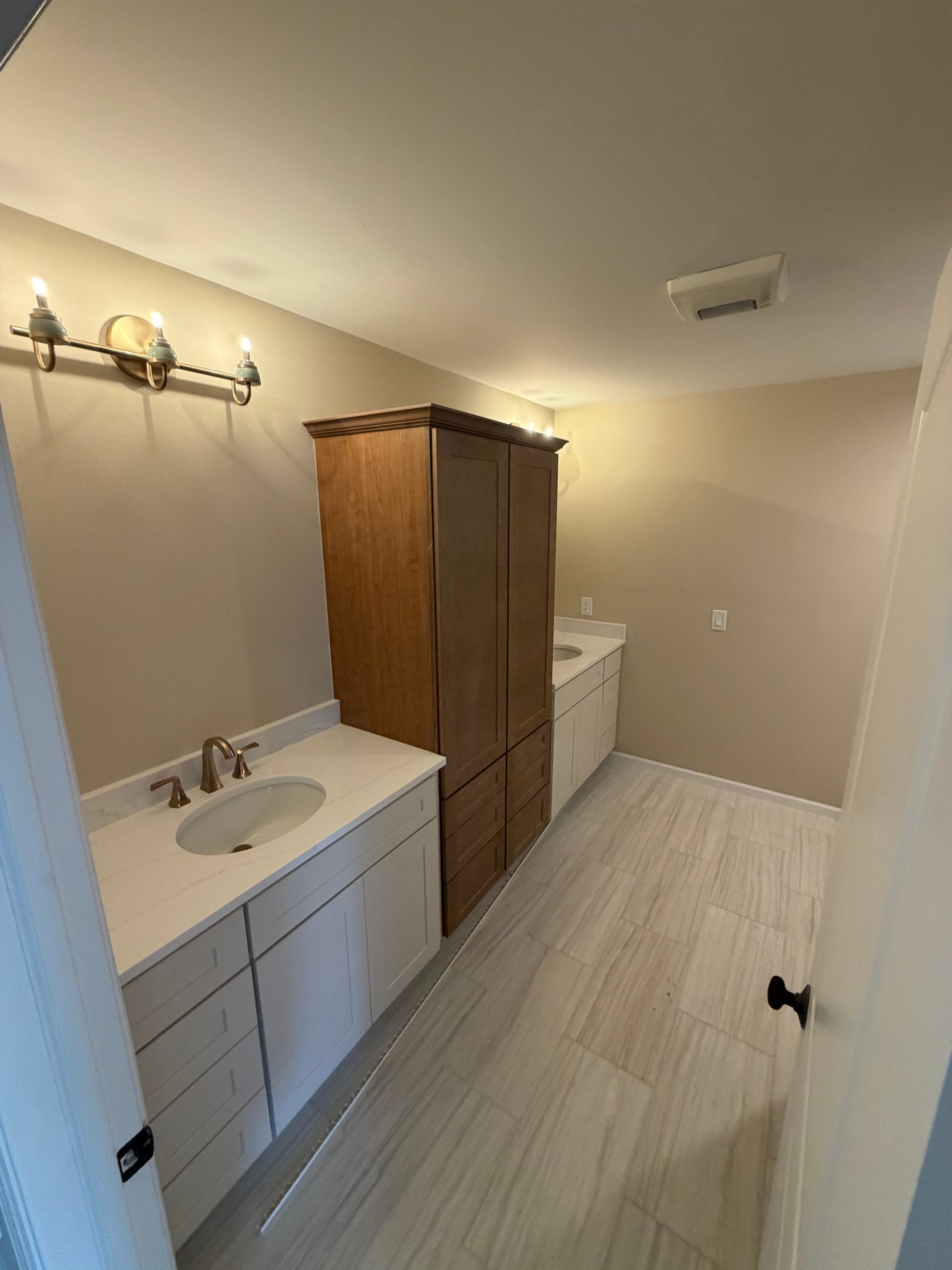 Small beige bathroom with white vanity, mirror light, wood cabinet, and washer/dryer in back.