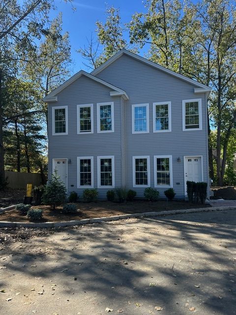 Two-story light blue duplex with white window frames and front doors, surrounded by trees.