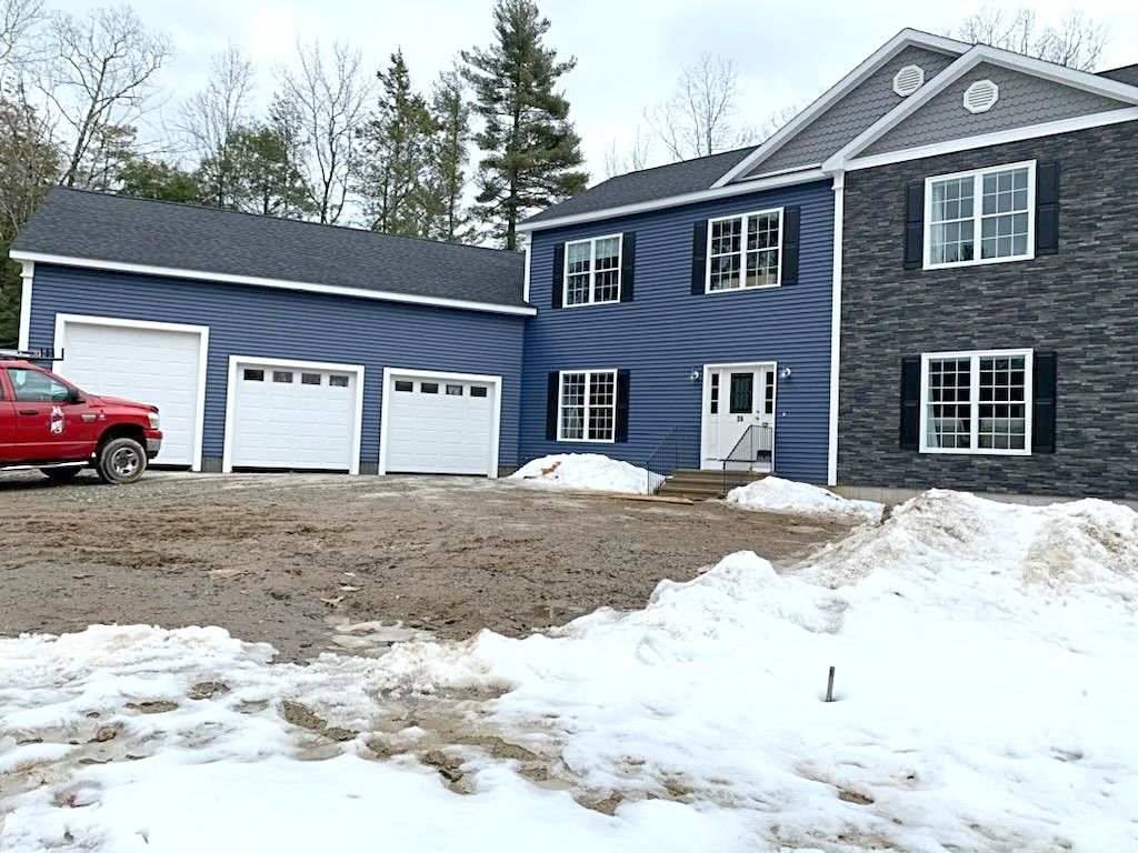 New house with attached garage; blue siding, dark gray accents, snow on ground, red truck.
