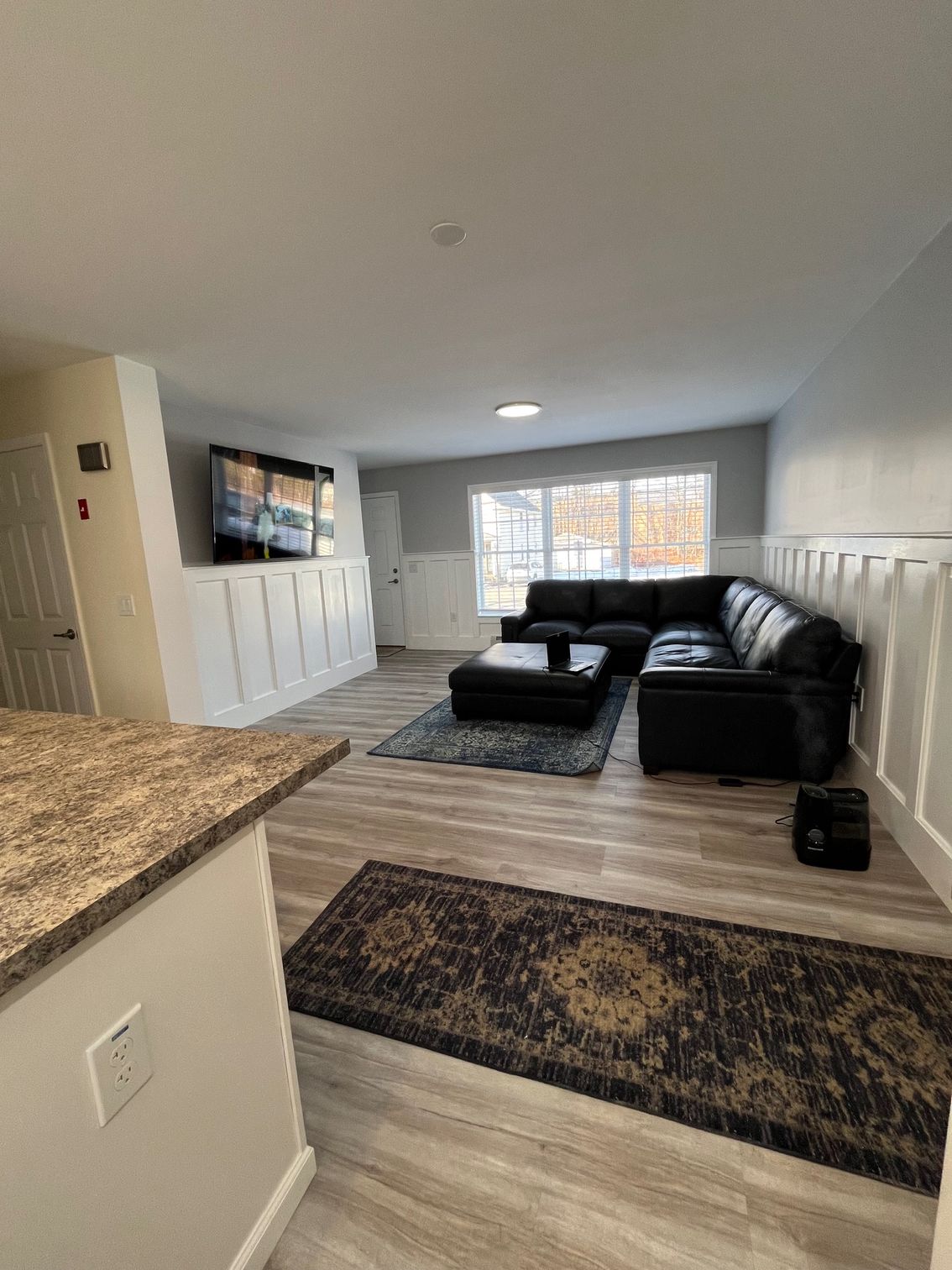 Living room with sectional sofa, TV, rugs, and wood-look flooring.