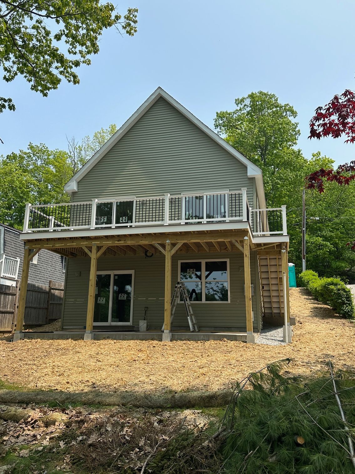 Two-story house with green siding and a wooden deck. The yard is covered in brown mulch.