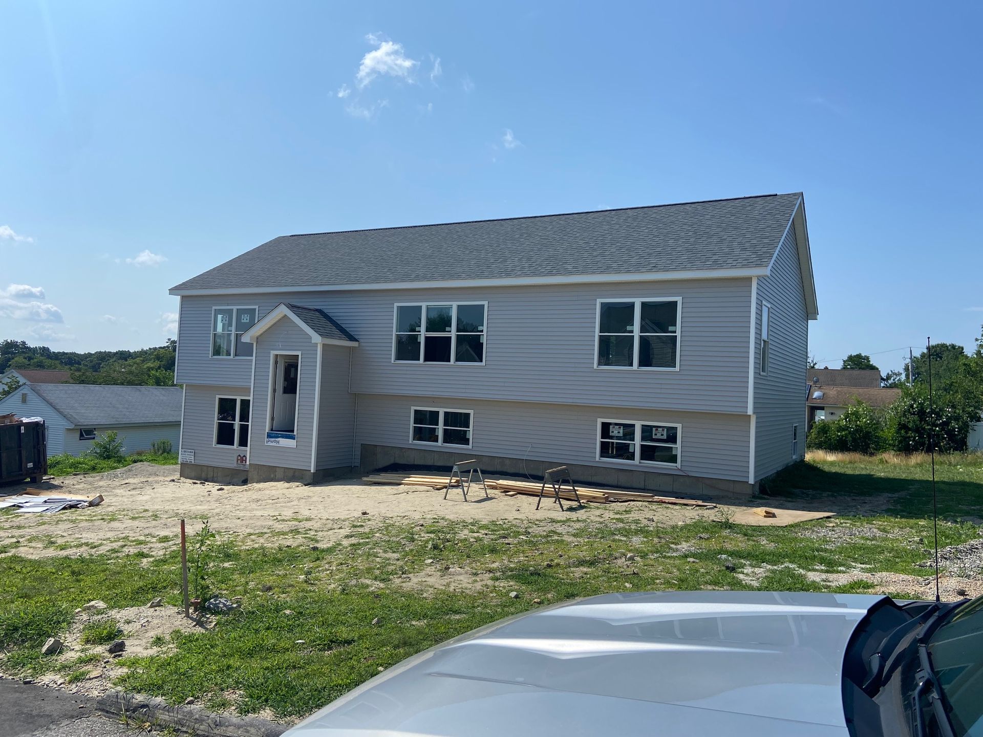 New two-story house under construction with gray siding and roof. Windows are installed, set on a sunny day.