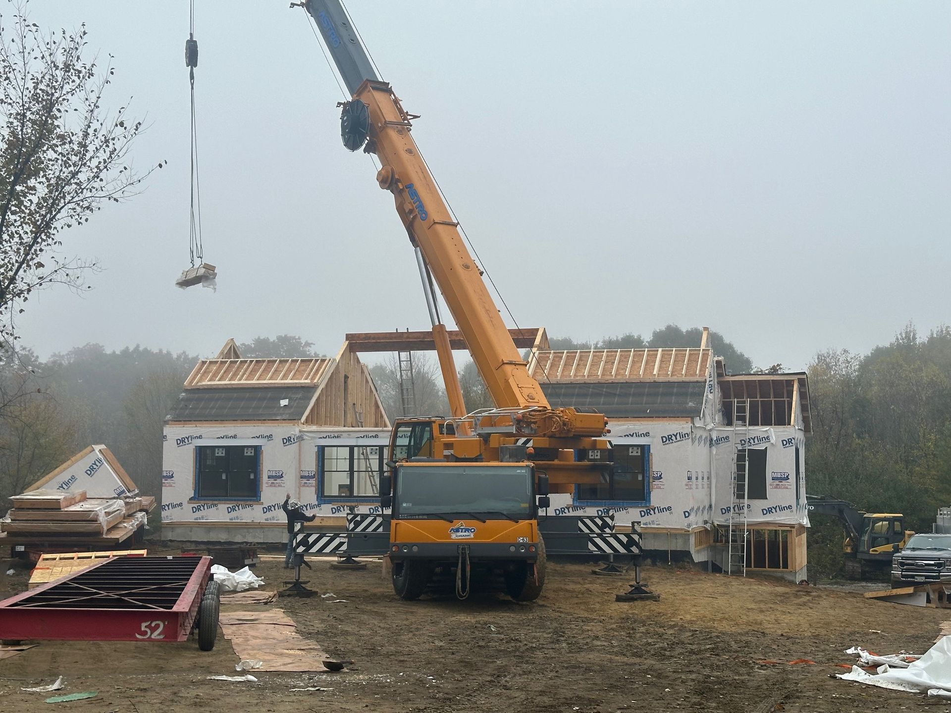 A yellow crane lifting a roof panel onto a partially constructed house on a cloudy day.