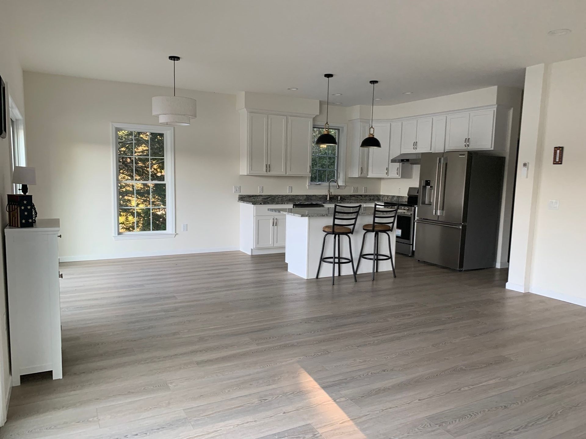 A bright open-concept kitchen with white cabinets, light wood floors, a center island with two stools, and a refrigerator.