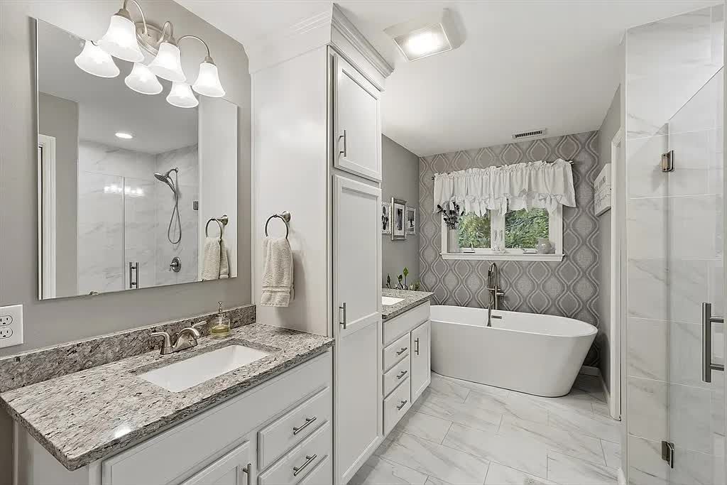 A modern bathroom featuring a white vanity with granite countertops, a standalone soaking tub, and a glass shower stall.