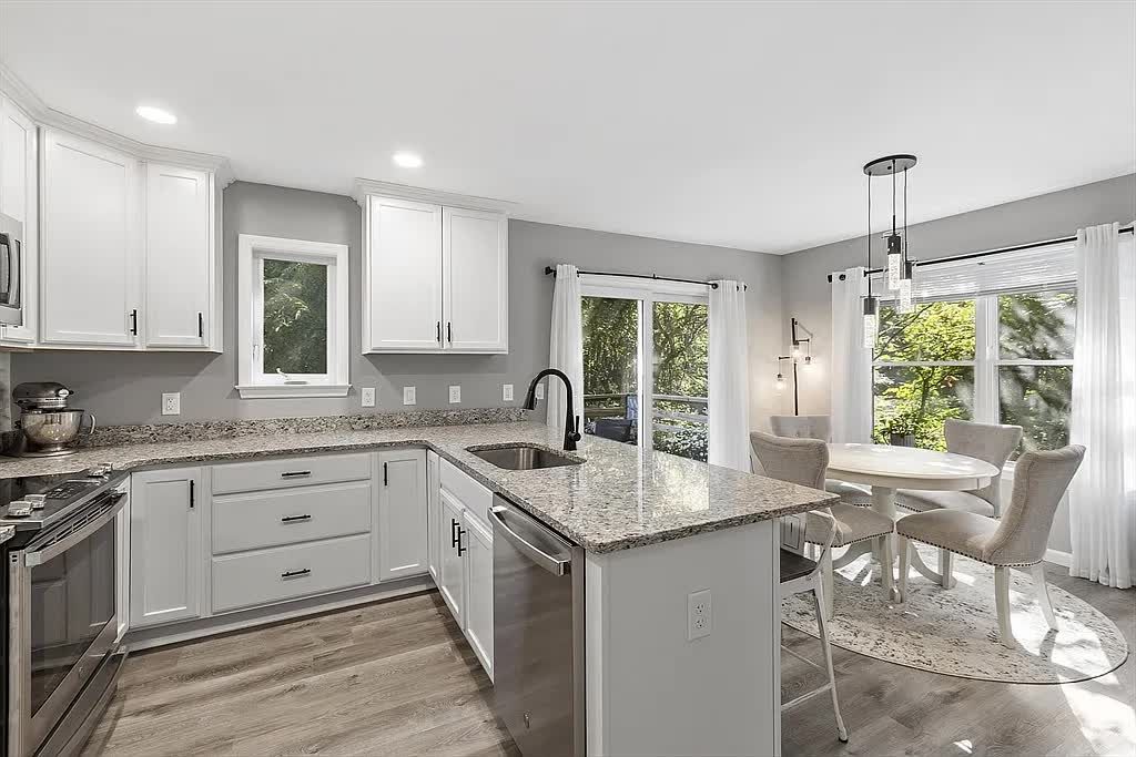 Bright, modern kitchen with white cabinets, granite countertops, a kitchen island, and a nearby dining table.