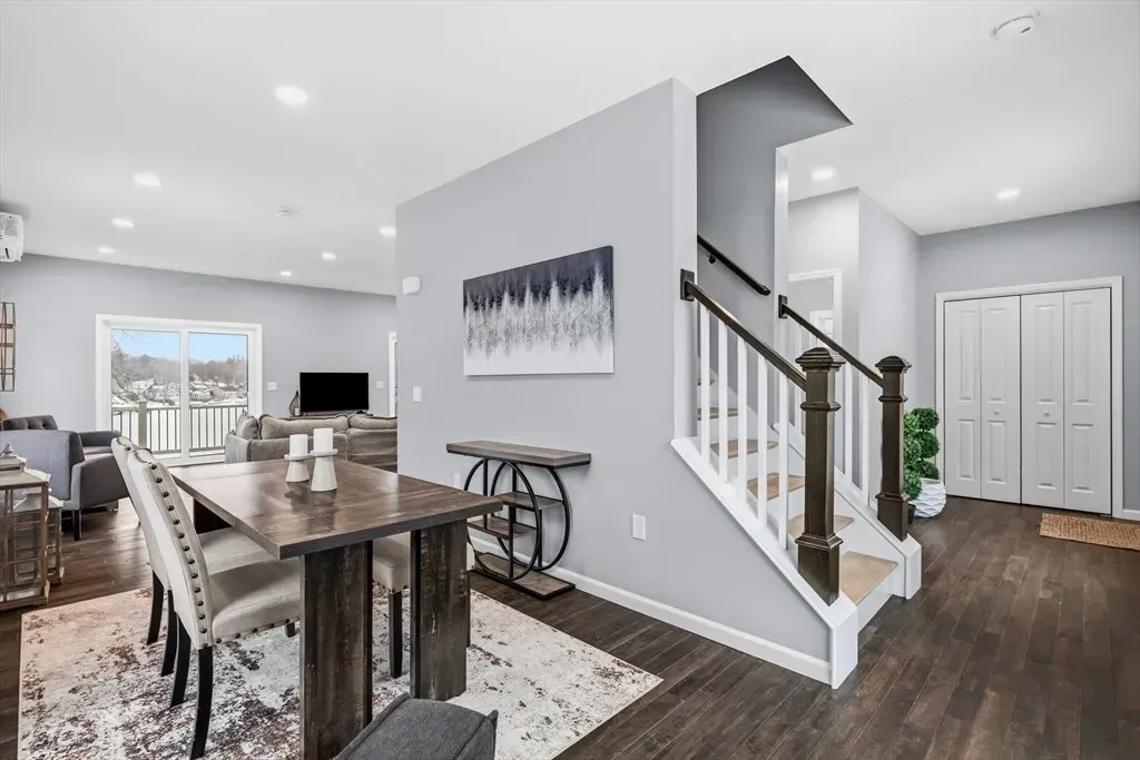 A modern open-concept home interior featuring a wood dining table, gray walls, a staircase, and light wood flooring.