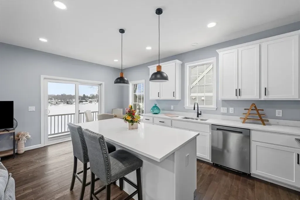 Modern kitchen with white cabinets, a large central island with two gray bar stools, and hardwood floors.