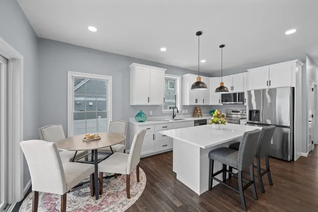 A bright, modern kitchen and dining area with white cabinets, a kitchen island, and a dining table with four chairs.