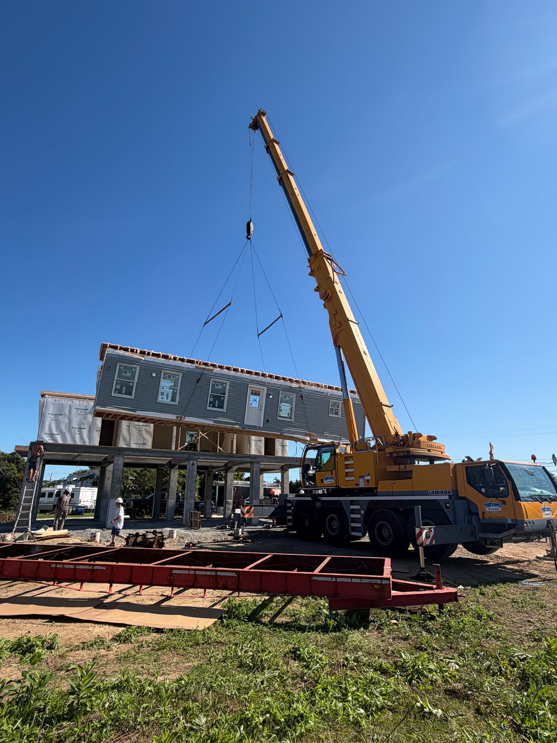 Yellow crane lifting a steel frame on a construction site under a clear blue sky