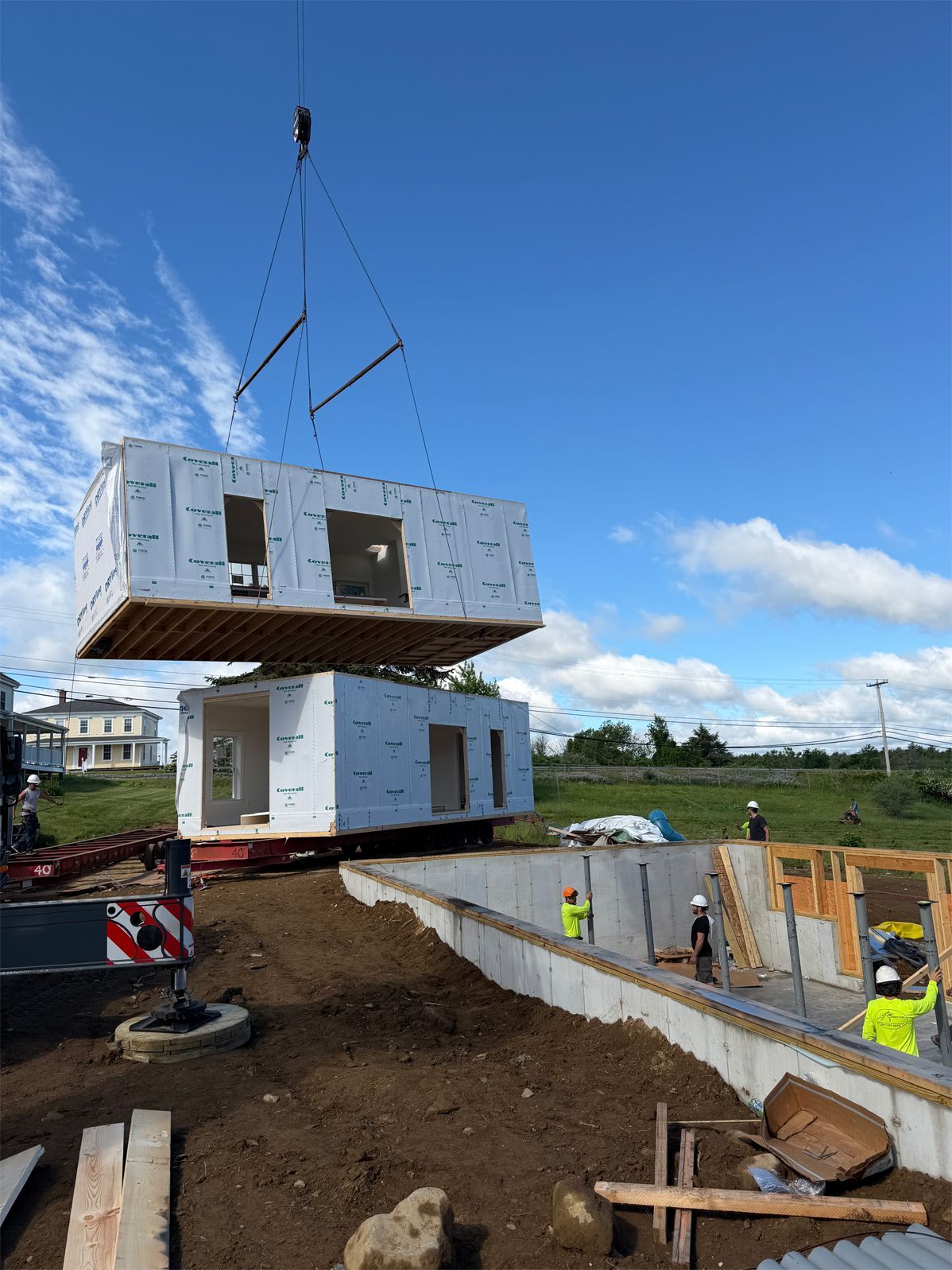 Crane lifting a white modular building section onto a foundation at a construction site