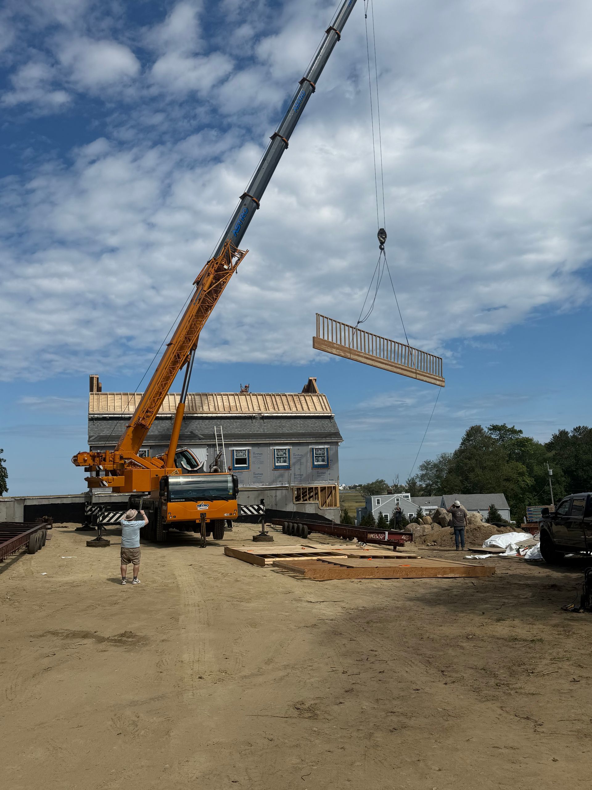 Crane lifting a metal frame at a construction site under a cloudy sky
